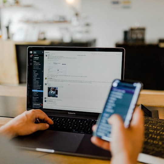 Working on a laptop with a banking app on the phone